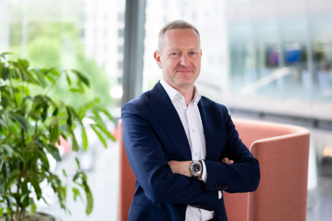 Portrait of Neil Bullen, Global Managing Director, Real Estate, In office standing by plant with his arms crossed.