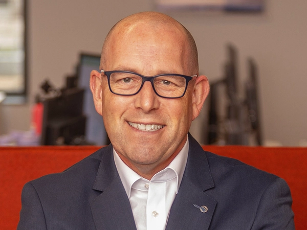 Portrait of Philip Matthews, Managing Director, Ireland, outside in front of a blurred brown background featuring a building and mix of natural and urban elements.