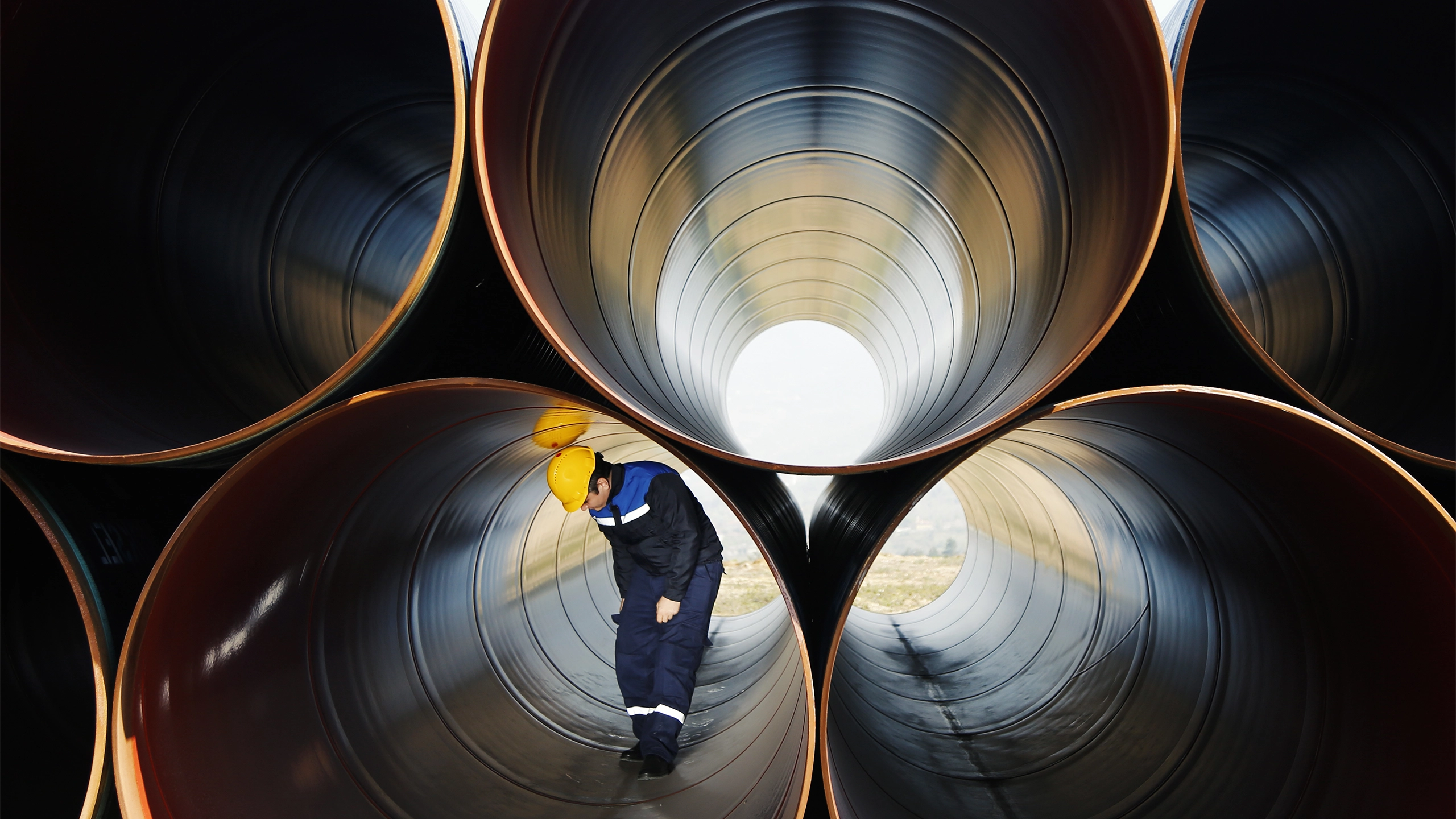 Man with yellow hard hat standing inside large cylinder 