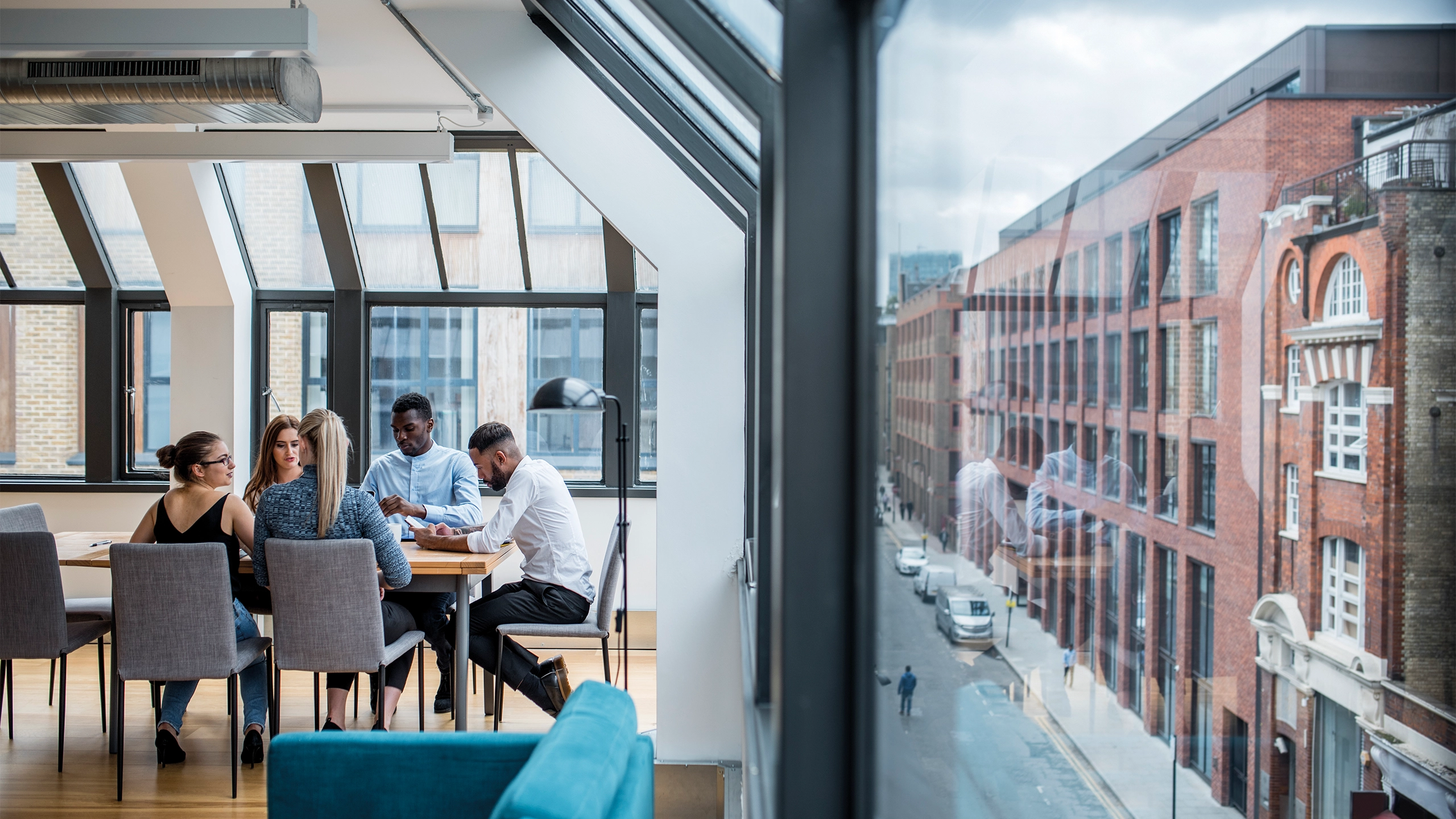 A group of male and female work colleagues sitting at a boardroom desk with exterior street view to the left