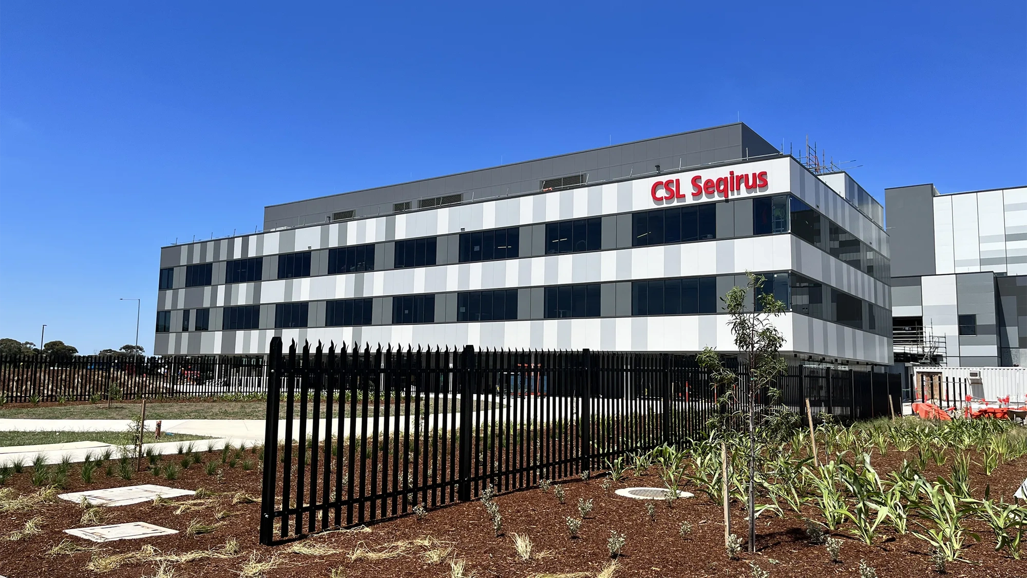 A CSL Seqirus vaccine facility, a multi-storey building set against a blue sky. 