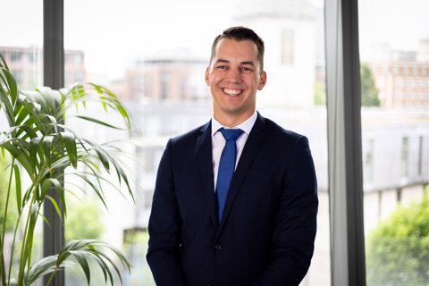 Portrait of Nicolas Offroy, Principal Consultant, Australia, standing in office space against window and plants.