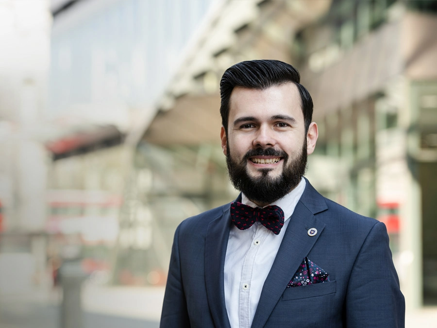 Adrian Predoi, Director, Head of Programme Advisory, Riyadh, Saudi Arabia, in a suit and bow tie smiling outdoors in front of a glass building