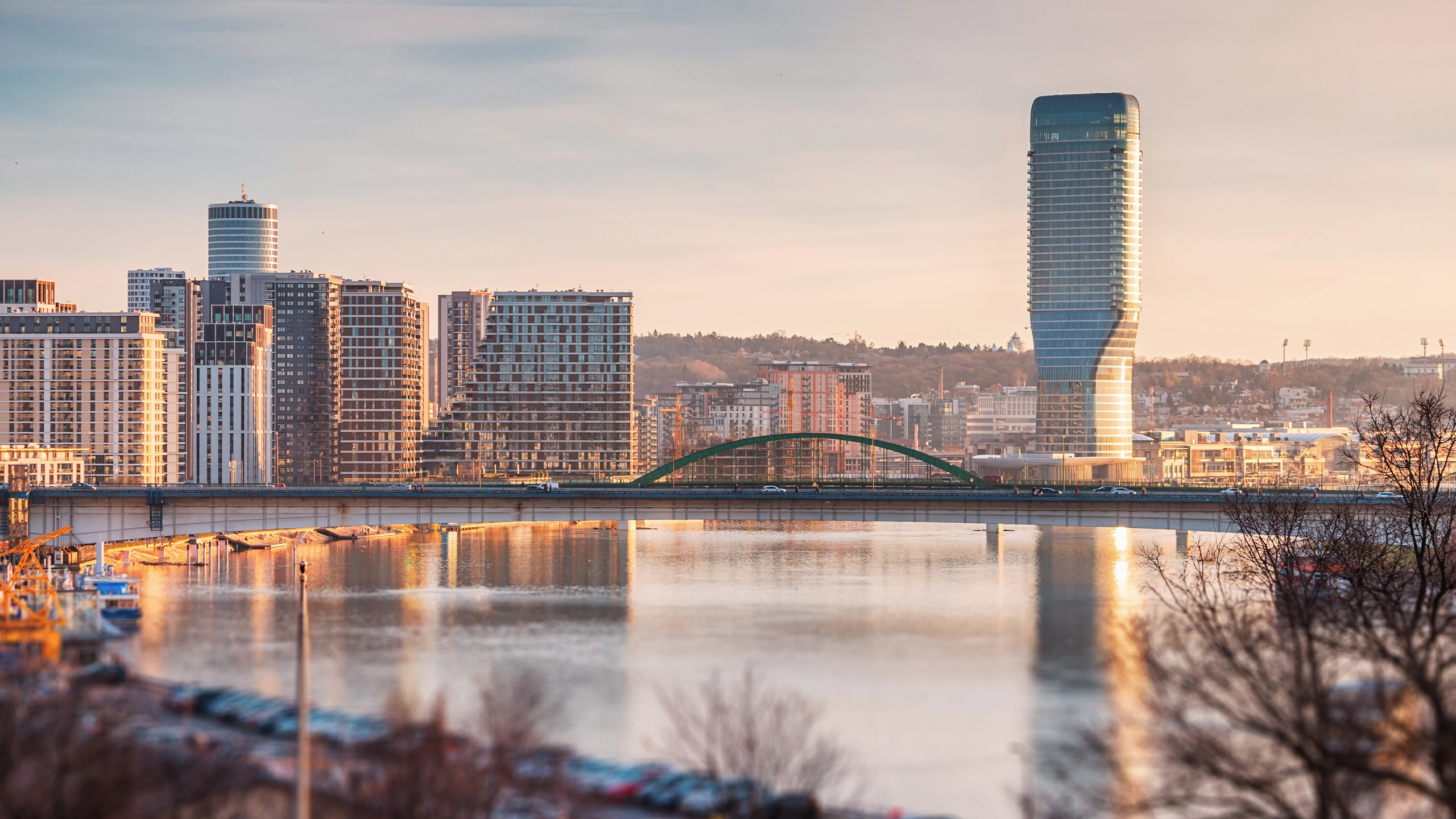 City skyline with modern high rise buildings and a bridge over a river at sunset.