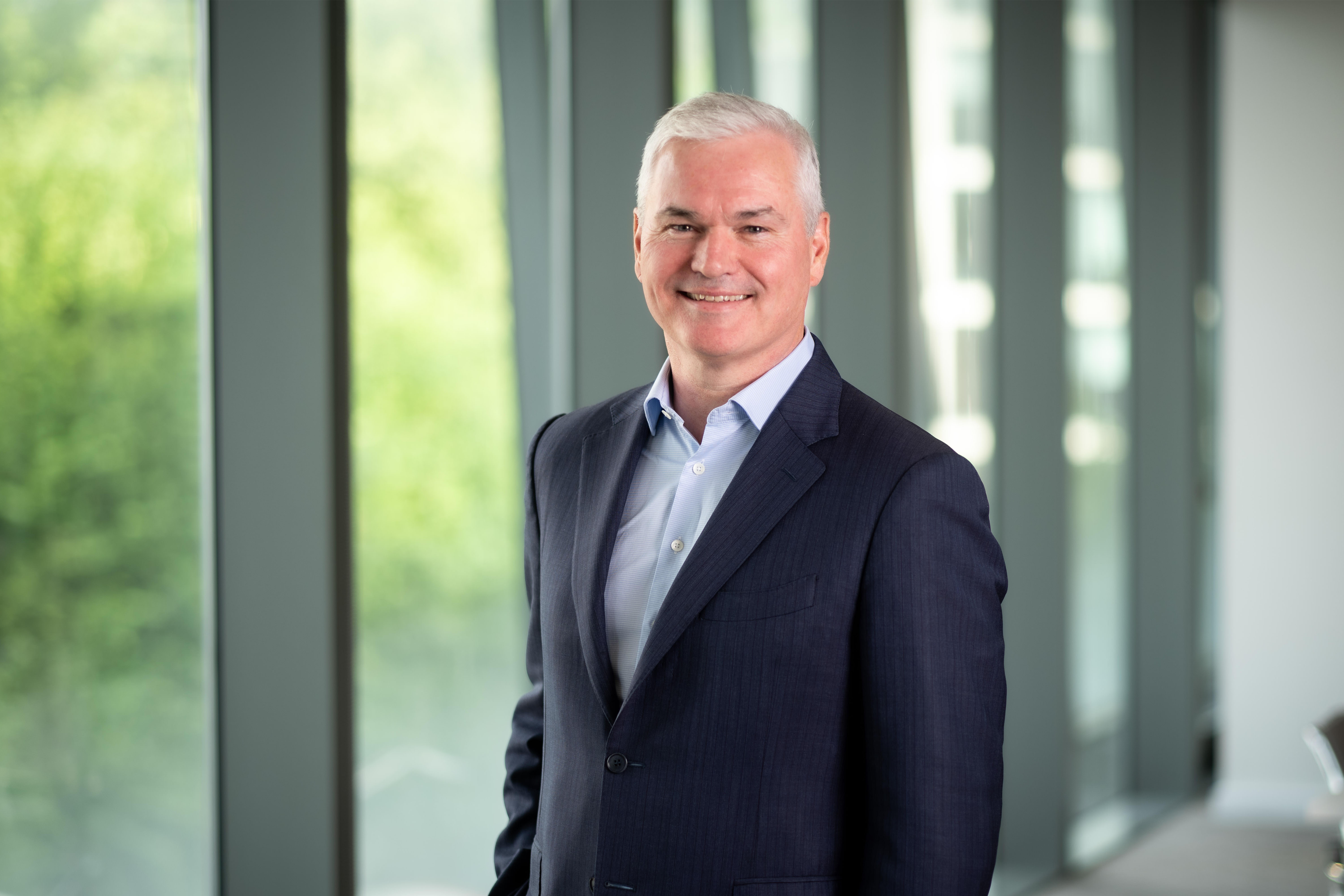 Vincent Clancy, CEO, smiling in front of a window with trees behind him