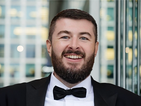 ortrit of Ash Boyle, Associate Director, standing in window based office building smiling.
