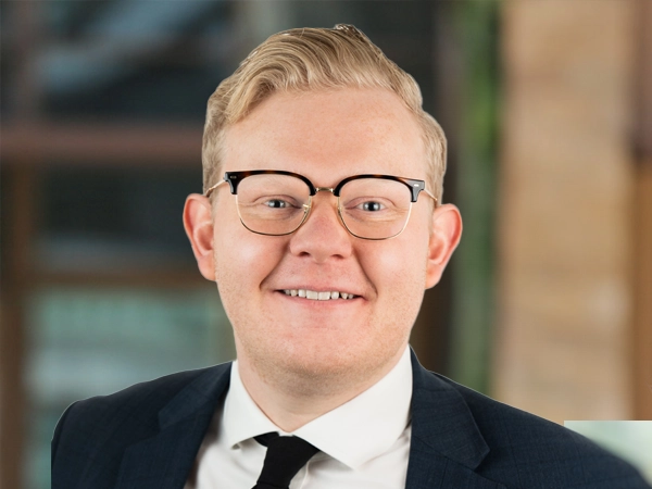 Ben Carter, Principal Consultant, UK, outside in front of a blurred brown background featuring a building and mix of natural and urban elements.