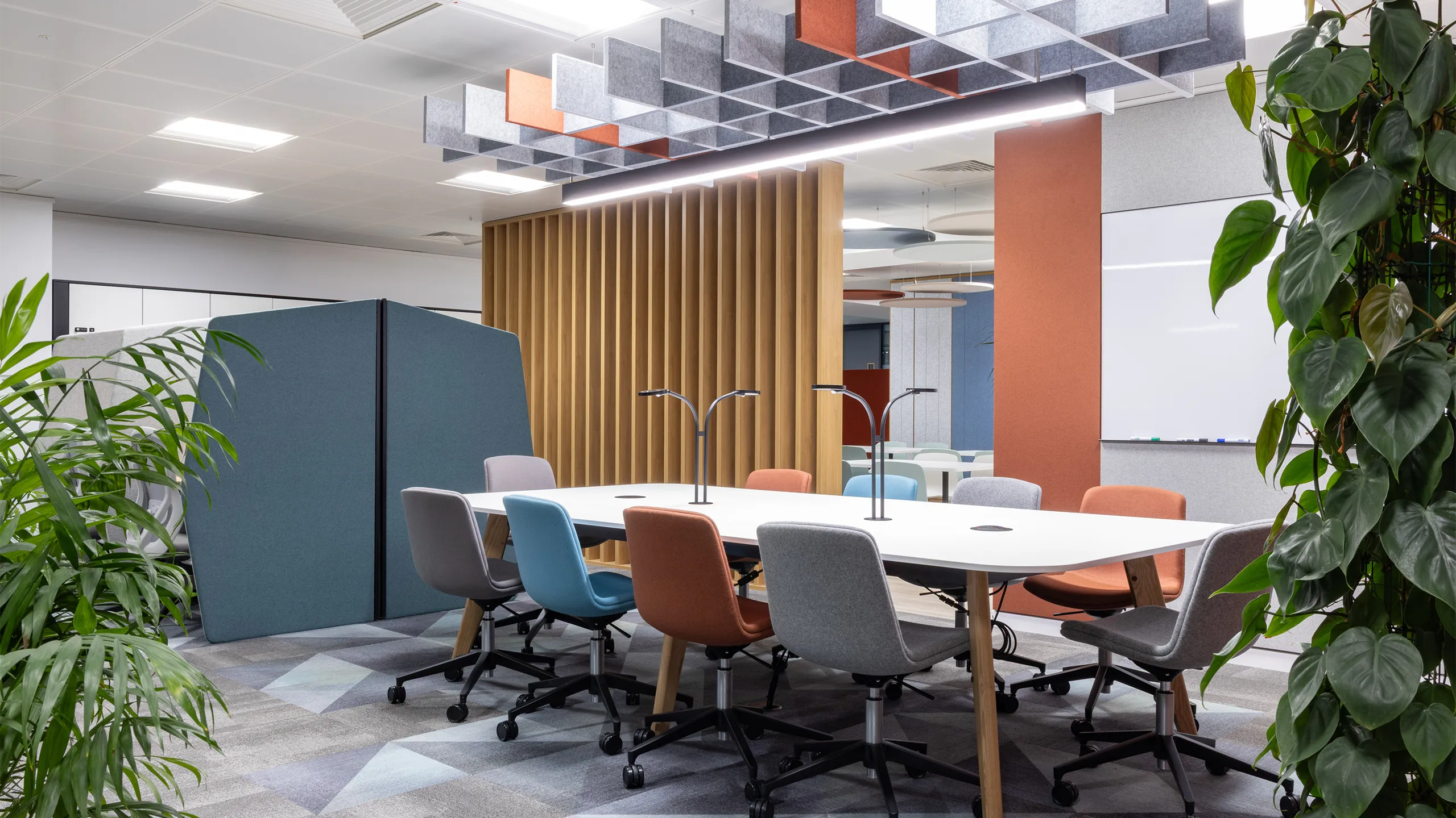  Turner & Townsend Bristol office. Plants in each corner with a meeting bank in the centre. There's colorful chairs around the table and a orange panel behind.
