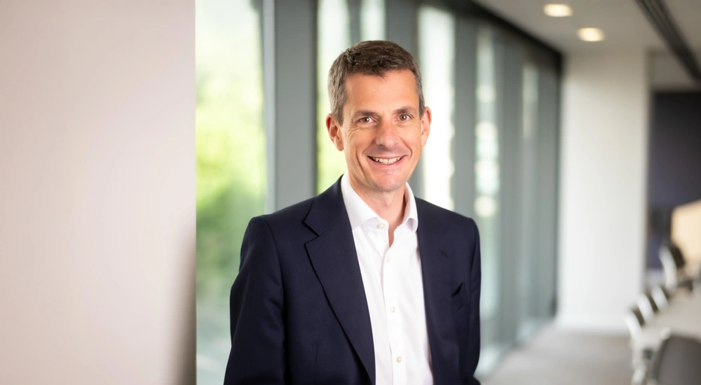 Finance Director, Richard Peers, smiling in an office interior in front of a window with trees