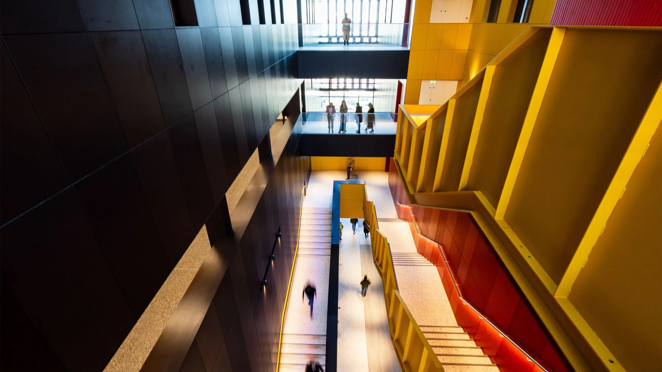 Yellow and red staircase in a black building with people chatting and walking down.