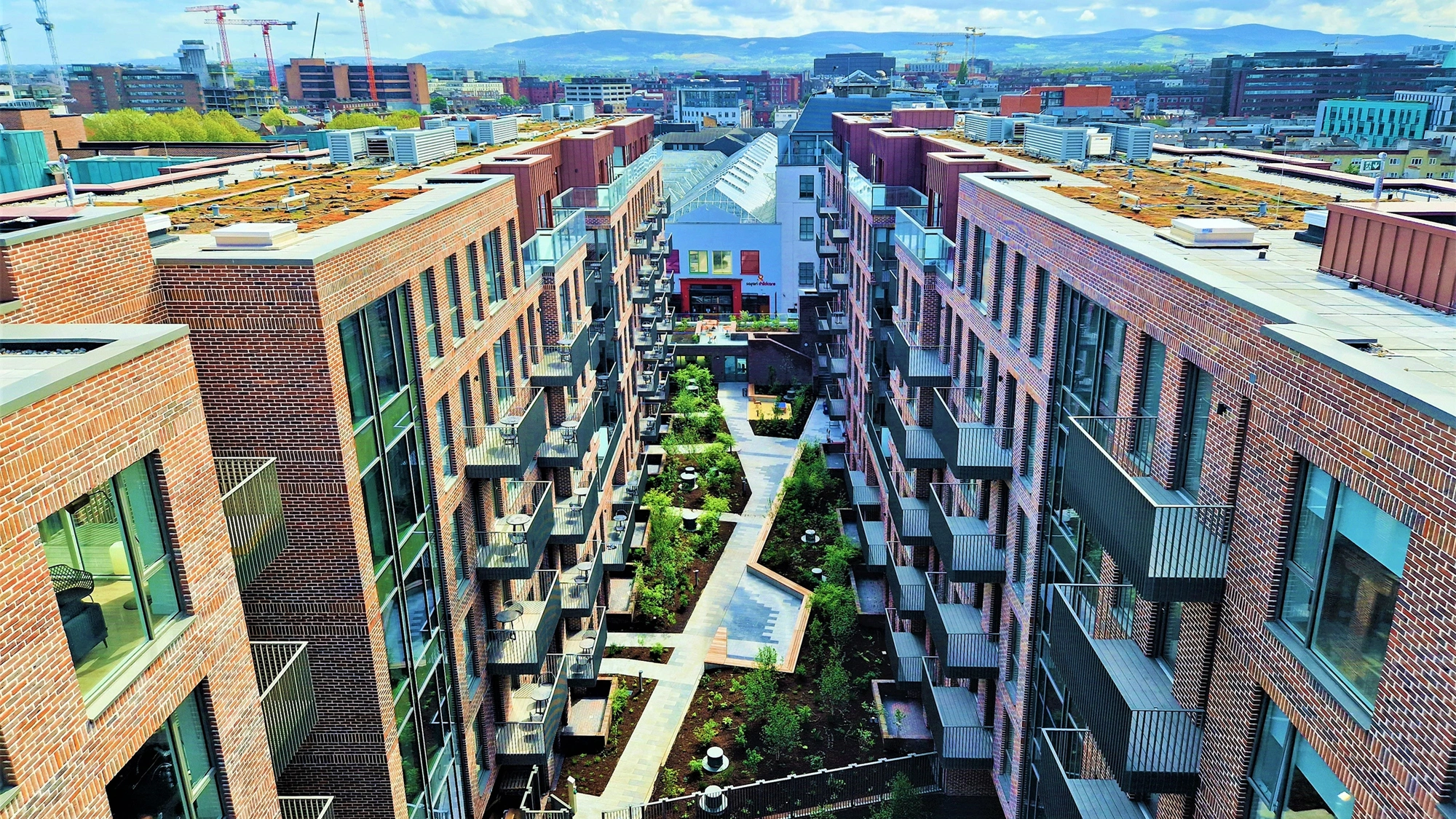 An aerial shot of a cluster of modern flats, with blue skies and small gardens. 