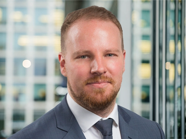 Portrait of Oliver Weir, Lead Project Manager, with city landscape featuring building with lots of windows in the background.