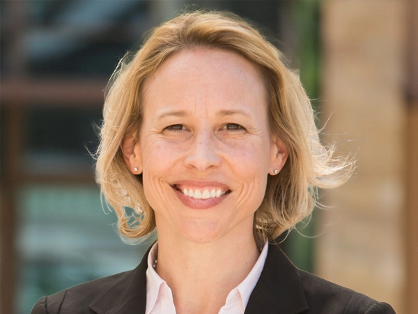 Lisa Woodruff, Executive Vice President, Global Head of Retail, outside in front of a blurred brown background featuring a building and mix of natural and urban elements.