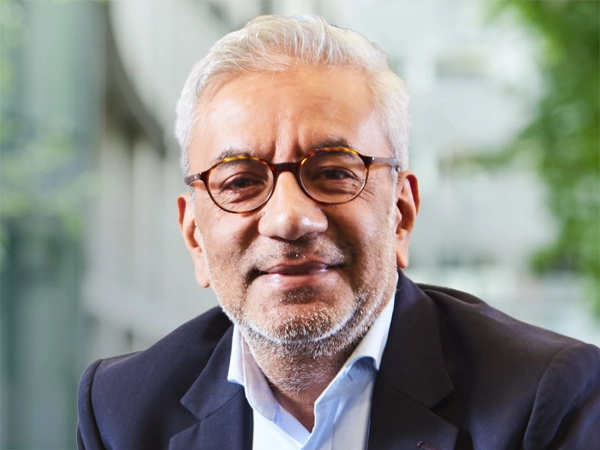 Nitesh Patel, Lead Economist, UK, standing outside in front of an outdoor urban setting, featuring modern architectural elements with clean lines. There are hints of greenery, suggesting some trees or plants.