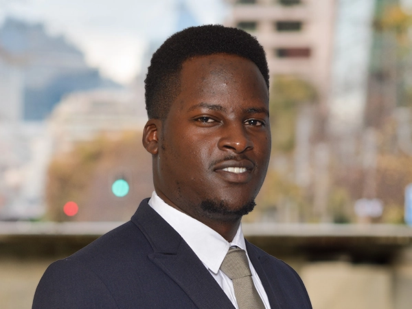 Portrait of Henry Wambaa, Project Manager, outside in front of a blurred brown background featuring a building and mix of natural and urban elements.