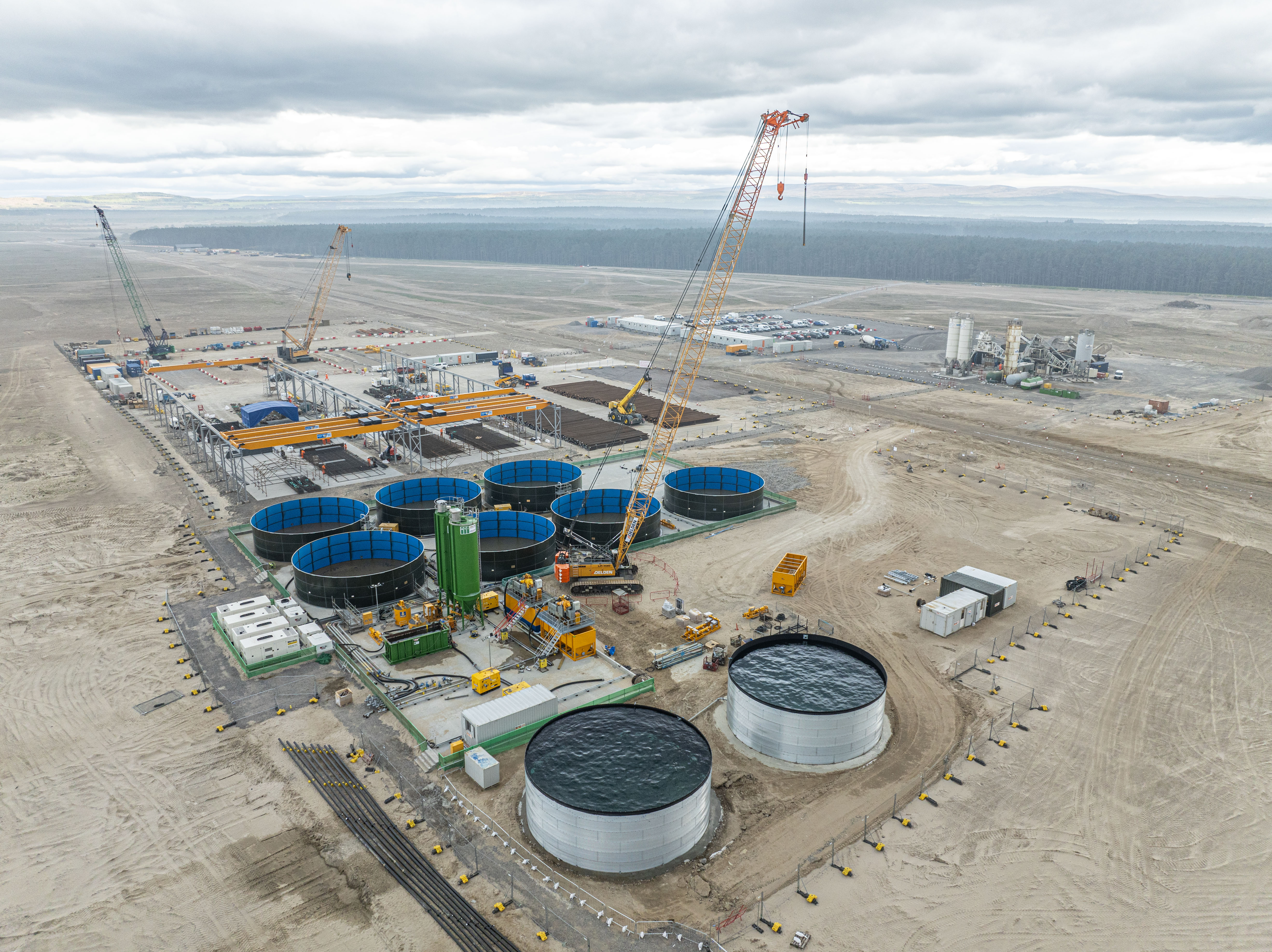 Aerial view of port buildings and storage facilities under construction in the foreground, looking out towards the sea in the distance