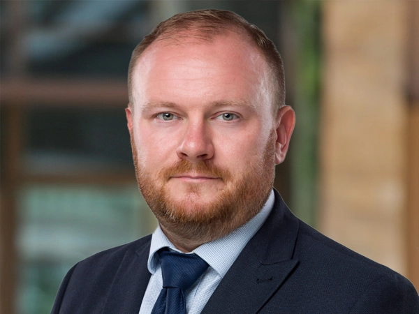 David Griffiths, Director, Real Estate Lead, UAE,  outside in front of a blurred brown background featuring a building and mix of natural and urban elements.