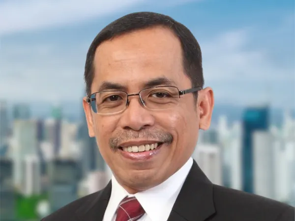 Portrait of Bayu Utomo, Director, Indonesia, outside in front of tall city buildings with blue skies.