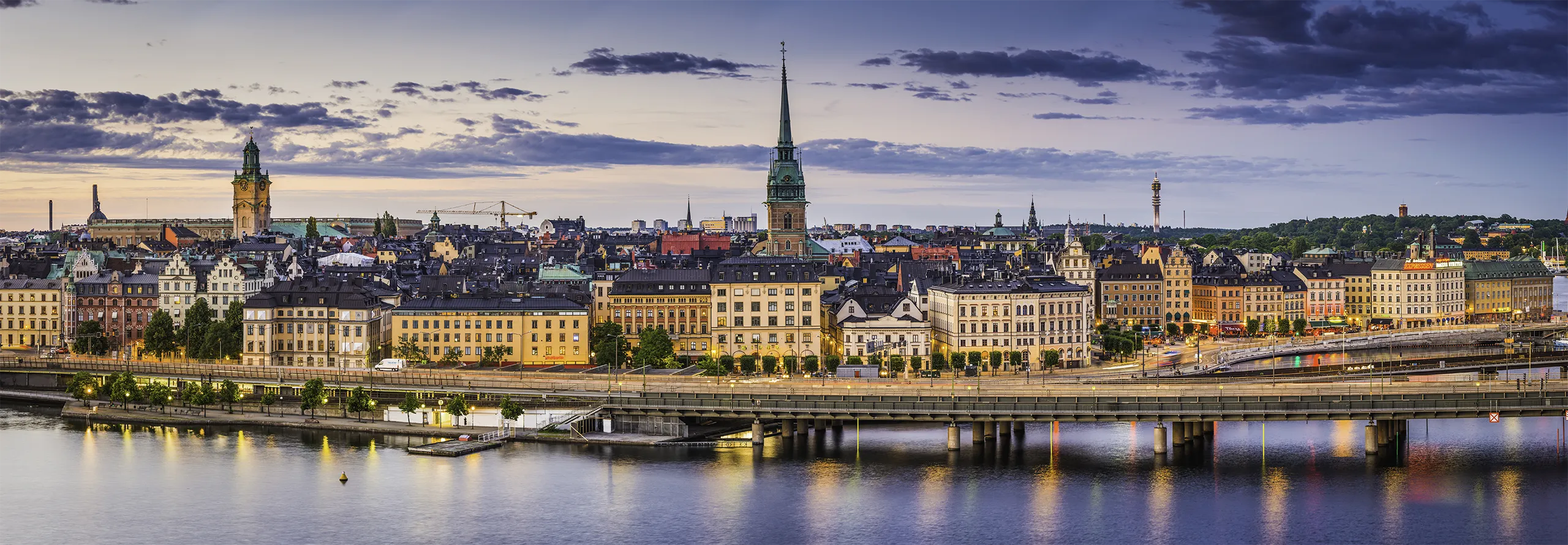 High angle panoramic view across the rooftops and spires of Gamla Stan as the dusk lights illuminate the heart of Stockholm, Sweden's vibrant capital city.