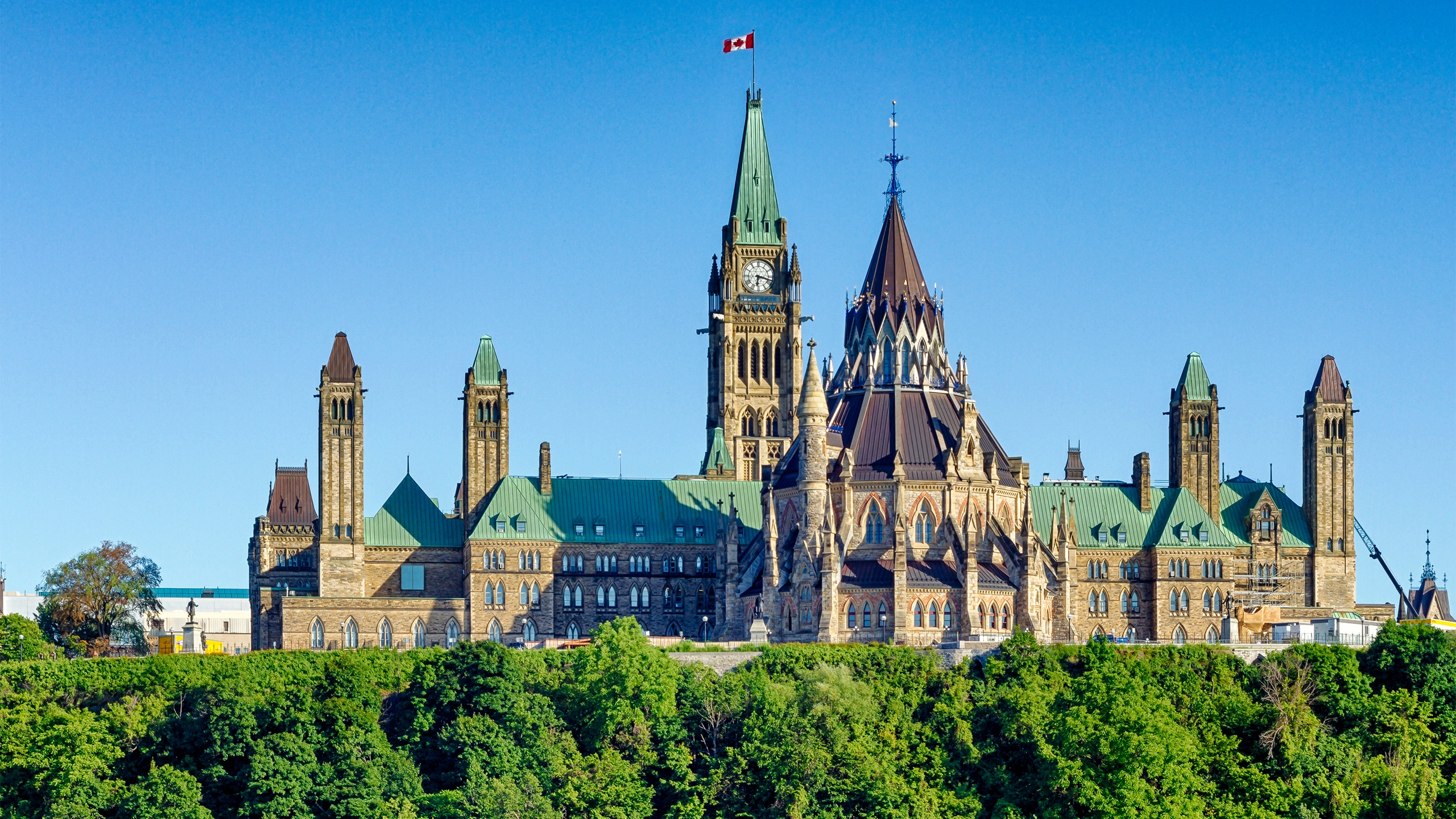 Parliament building in Ottawa, Canada with clock tower flying Canadian flag against a blue sky