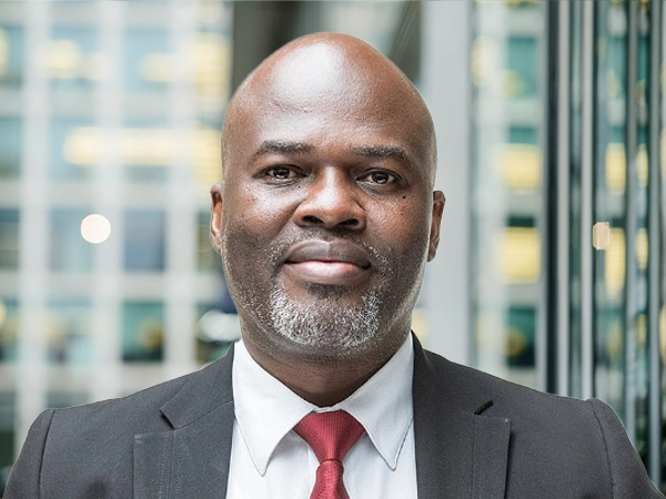 Portrait of Eric Ousoh, Senior Project Manager, with city landscape featuring building with lots of windows in the background.