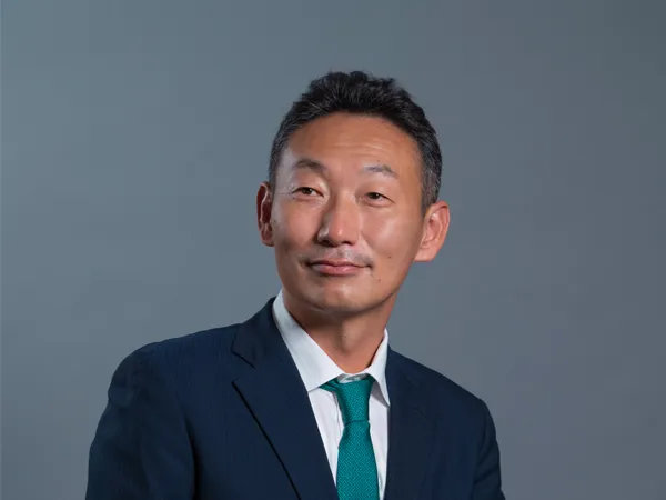 Portrait of Kajiura Hisanao, Managing Director, Japan, in blue suit against dark blue/grey background.