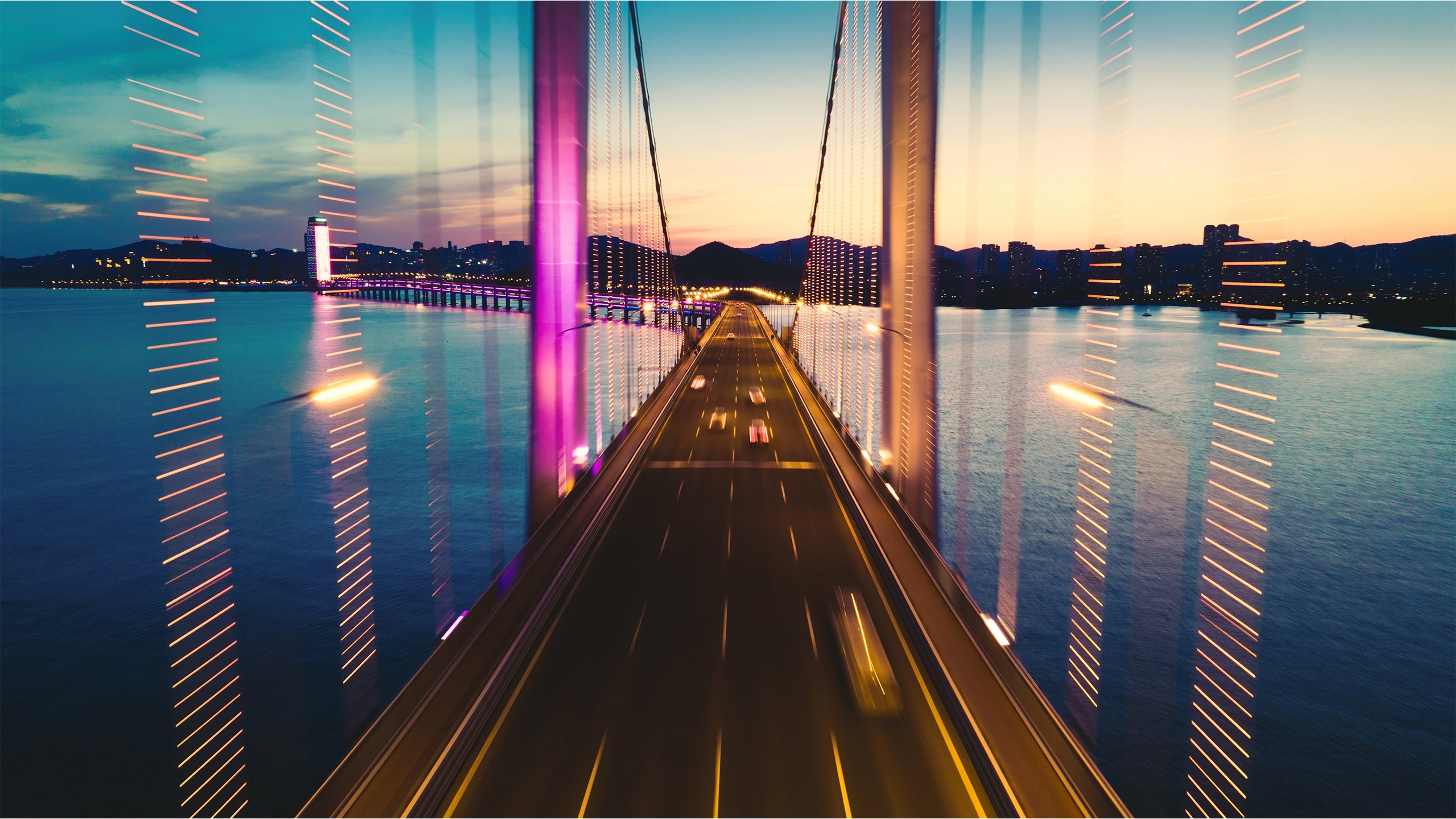 Road bridge over wide river at night with mountains in the background
