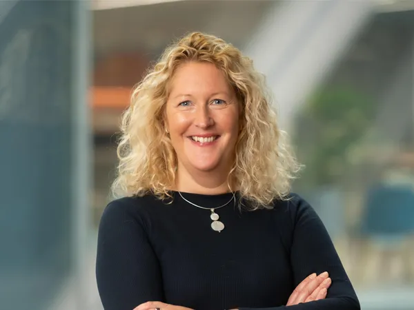 Portrait of Vicky Shepherd, Associate Director, UK Communications, standing with arms folded in office smiling