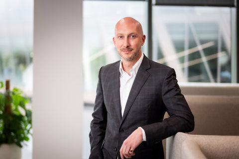 Portrait of James Hardy, Director, Head of UK Sustainability, standing in office space next to plant.