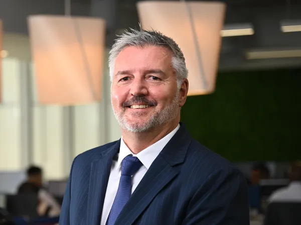 Portrait of Kobus Havemann, Country Manager, Smiling in blue suit in blue themed office space.
