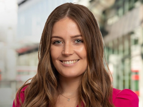 Georgina Bonney, Senior Sustainability Consultant, standing outside in front of buildings featuring an urban cityscape with a mix of architectural styles. The scene includes some windows and red features, adding a touch of color.