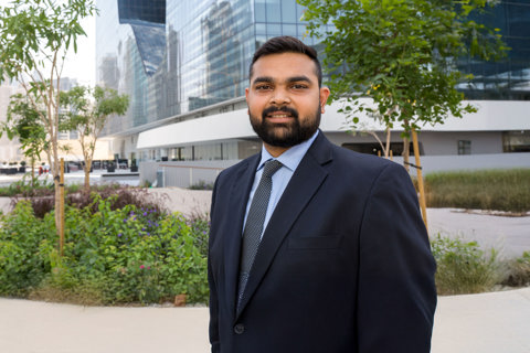 Portrait of Ranjeet Pundlik, Associate Director, Project Management, Dubai, outside in front of tall city building with glass windows.