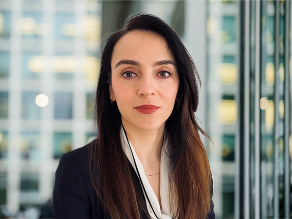 ortrait of Gabriela Mariniuc, Associate Director, standing in window based office building smiling.