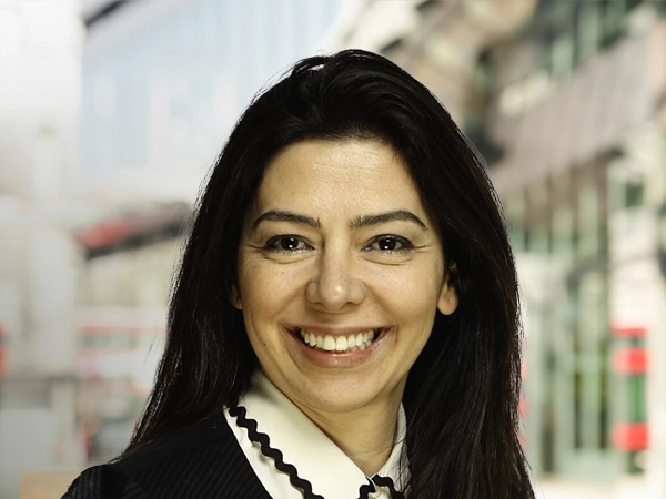 Portrait of Diana Unterstrasser, Director, Europe, Occupier and Retail, standing outside in front of buildings featuring an urban cityscape with a mix of architectural styles. The scene includes some windows and red features, adding a touch of color.