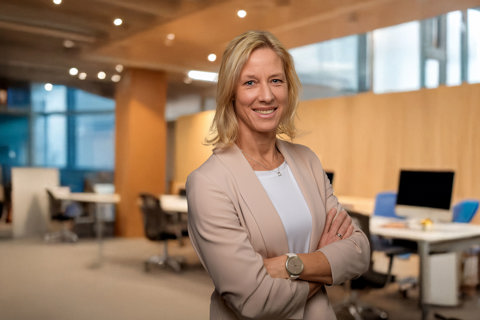 Portrait of Bettina Würfel, Managing Director, standing in an office with warm wooden backdrop and windows